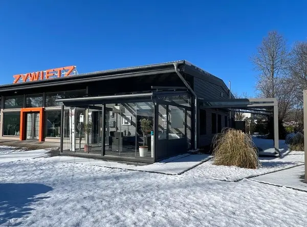 Modernes Firmengebäude mit Wintergarten und Schnee im Außenbereich bei blauem Himmel.