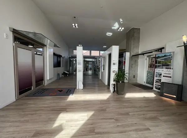 Moderner Ausstellungsraum mit großen Fenstern, Holzboden und Präsentation von Bauelementen.