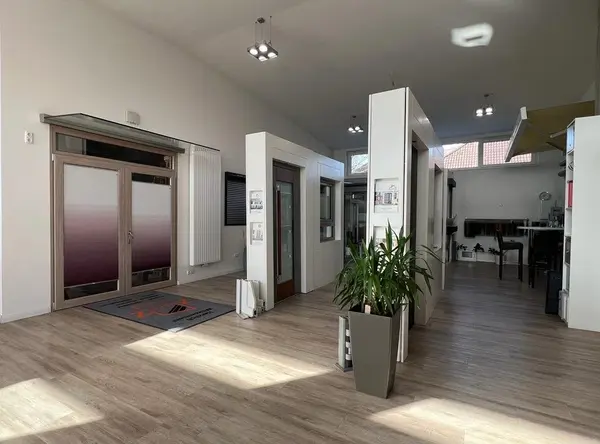 Moderner Ausstellungsraum mit Fenstern, Türen, Sonnenschutz und heller Inneneinrichtung.