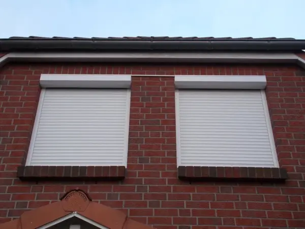 Zwei geschlossene Rollläden an roten Klinkerfenstern eines modernen Einfamilienhauses.