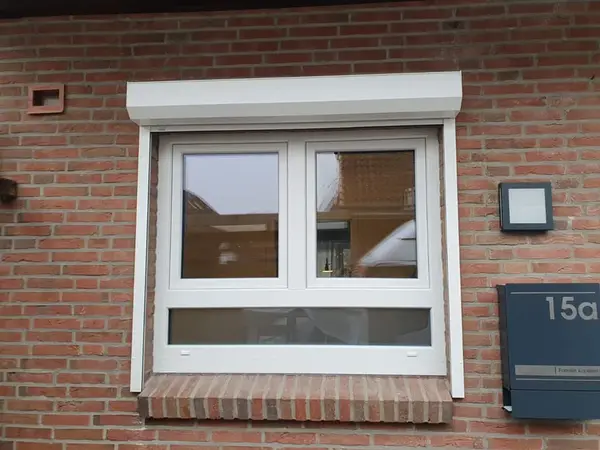 Modernes weißes Kunststofffenster mit Rollladen an roter Klinkerhausfassade und Hausnummer.