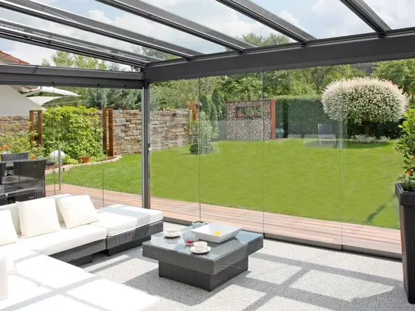 Moderner Wintergarten mit Glasdach und gemütlicher Sitzecke bietet Blick in Garten.