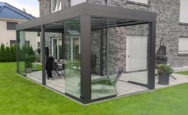 Moderne Terrassenüberdachung aus Glas mit Aluminiumrahmen an einem Einfamilienhaus im Garten.